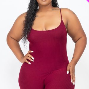 A smiling plus-size woman wearing a tight-fitting, ribbed knit romper with spaghetti straps. The one-piece garment hugs her curves and the fabric has a vertical texture.
